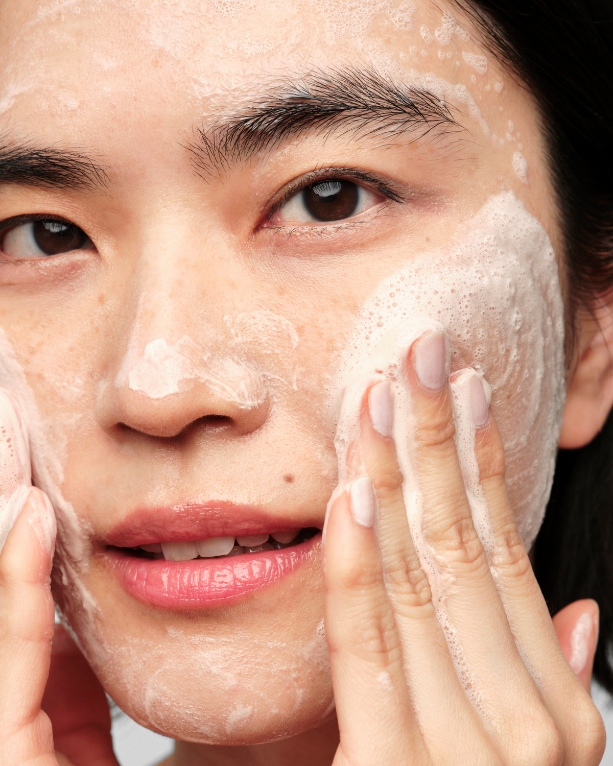 A person massaging the Skinfix Balancing Soft-Foam Clay Cleanser into their face, with a rich foam lather visible across the skin.