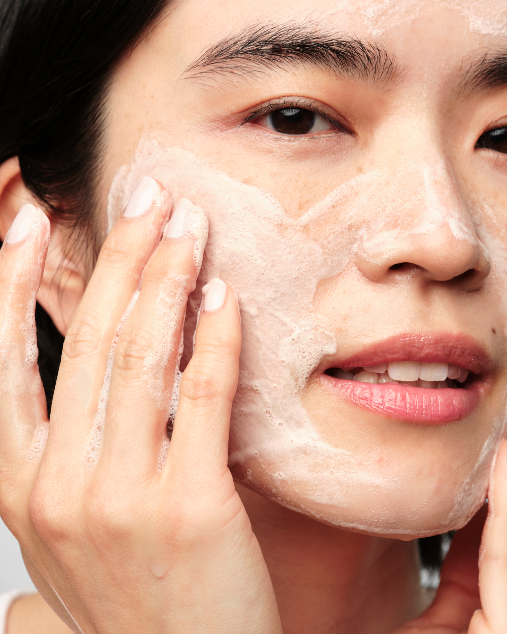 A person massaging Skinfix Balancing Soft-Foam Clay Cleanser onto their face, showing the product's soft, foamy lather.