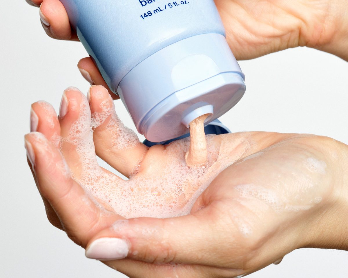 Skinfix Balancing Soft-Foam Clay Cleanser being dispensed into a cupped hand, showing the product's soft, foamy lather.