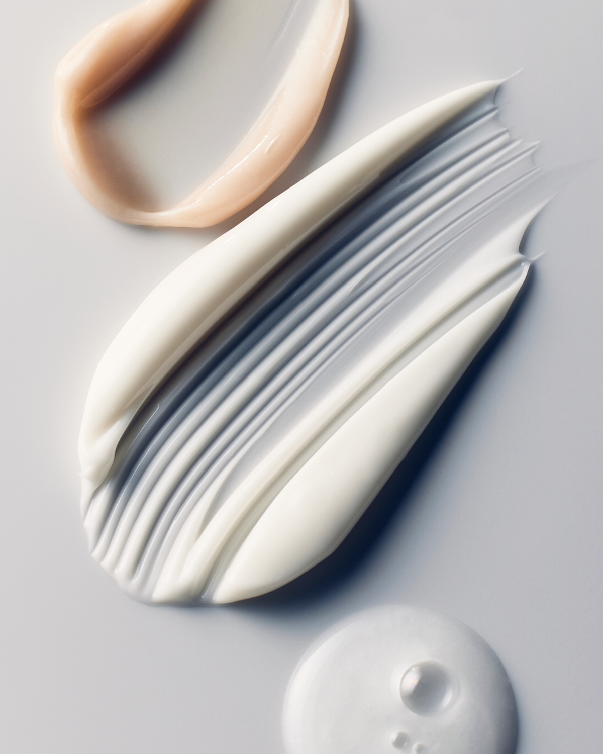 3 Skinfix product texture swipes. The top shows a beige, creamy texture. The middle shows a white rich texture. The bottom shows a white, foamy texture.