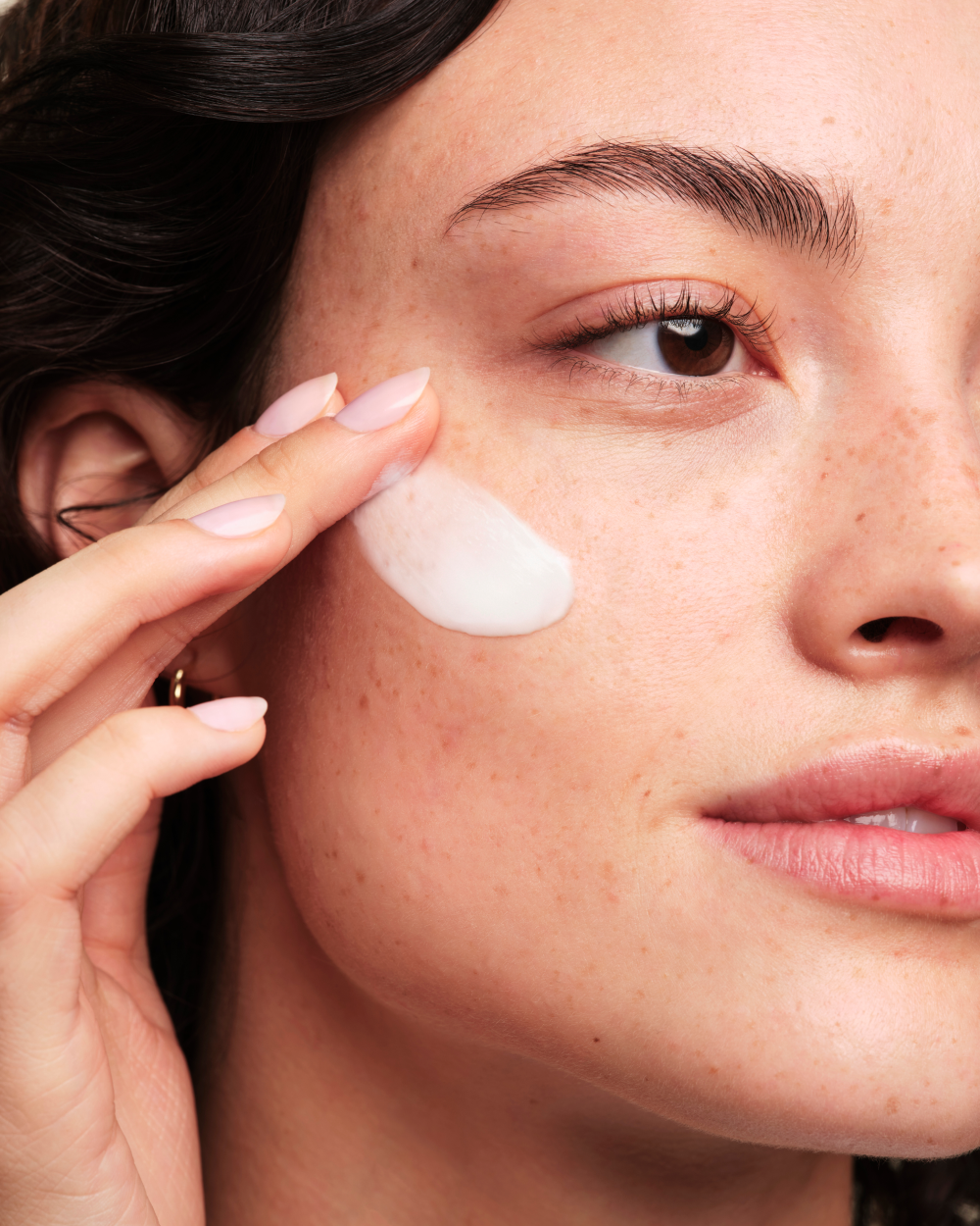 A person applying Skinfix Triple Lipid-Peptide Cream to their cheek.
